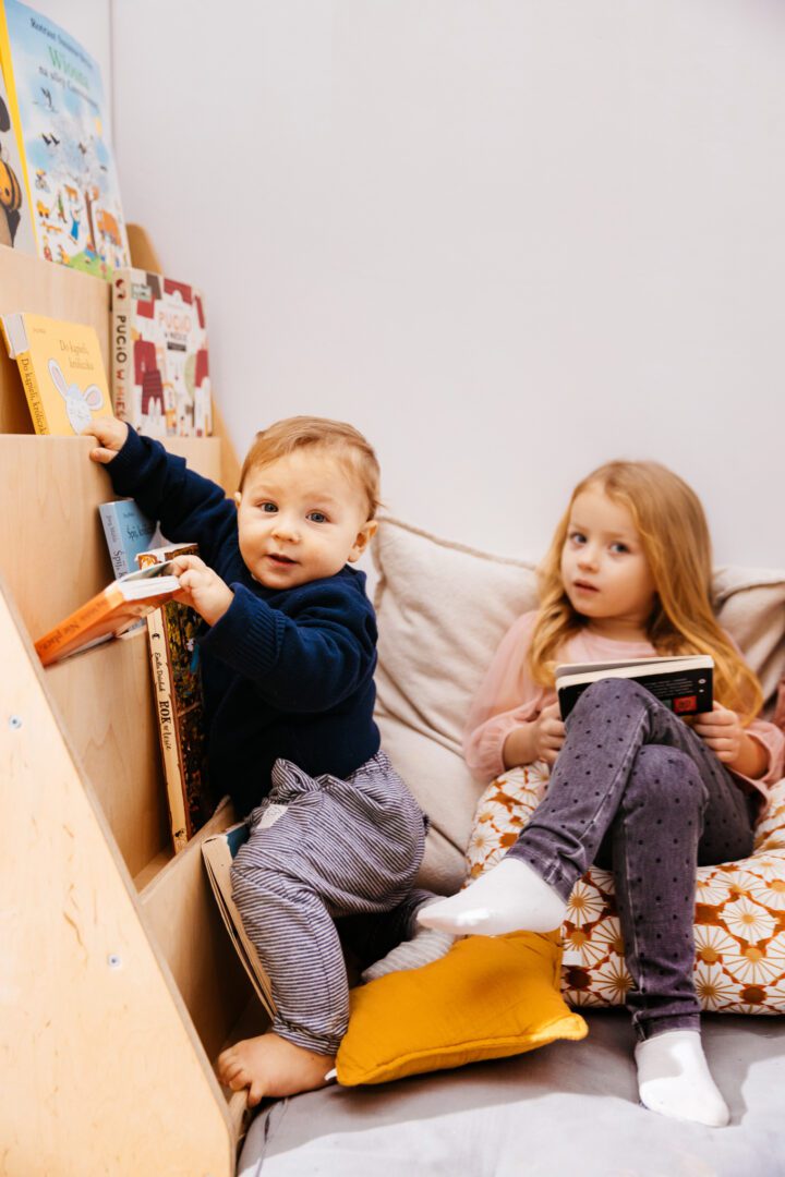 Chłopiec i dziewczynka siedzą przy biblioteczce z książkami