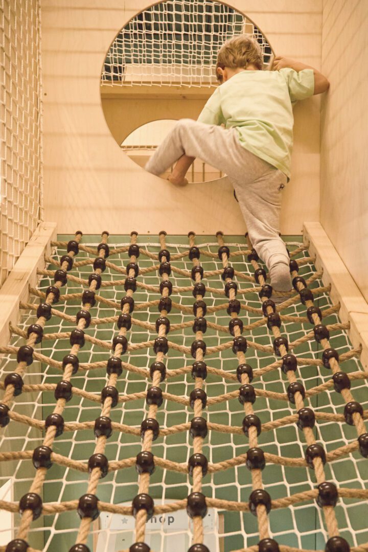 Chłopiec wspiął się na górę siatki wspinaczkowej i przechodzi przez okrągłe przejście w małpim gaju