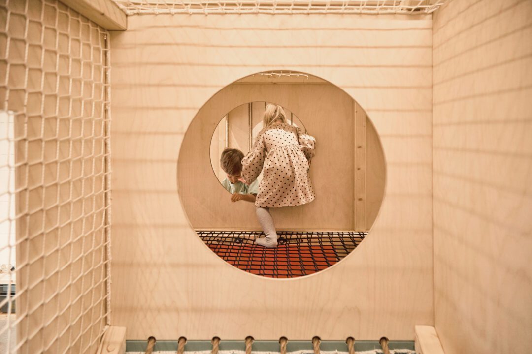 Dziewczynka i chłopiec przechodzą przez okrągłe przejścia wewnątrz drewnianej sali zabaw