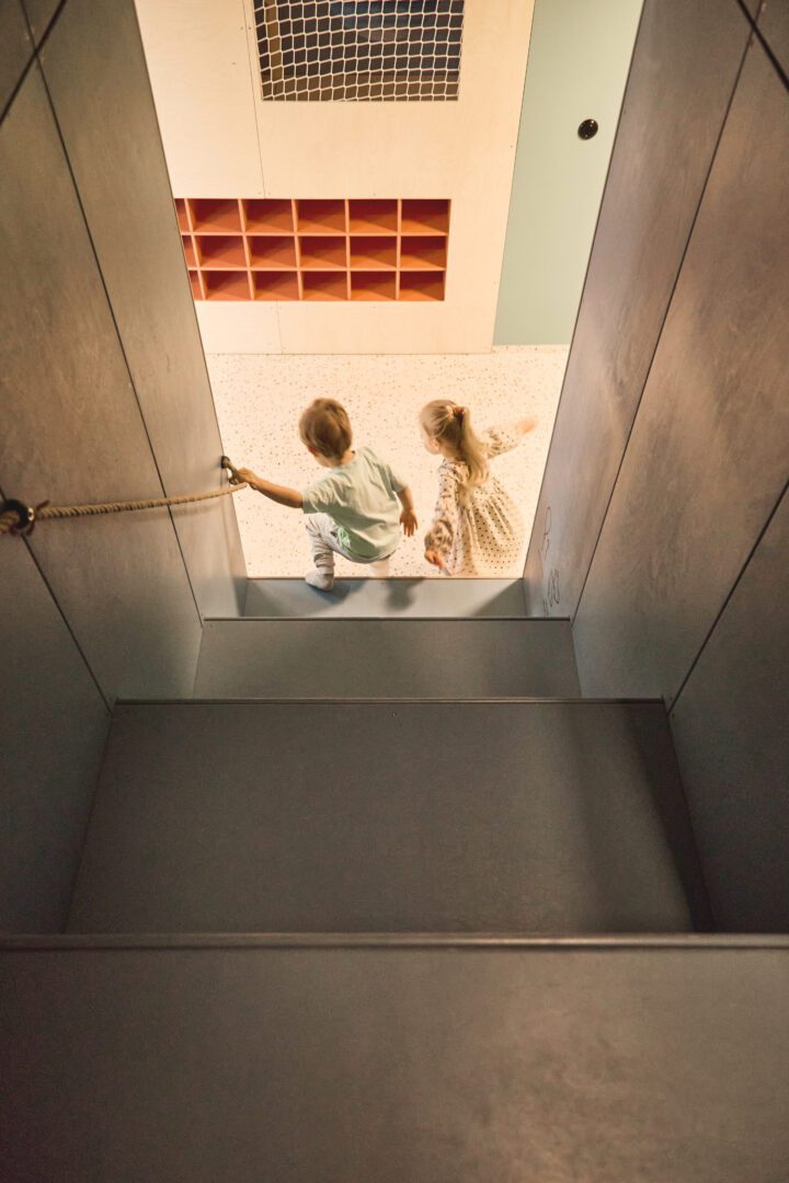 Chłopiec i dziewczynka schodzą ze schodów, chłopiec trzyma się sznurka pełniącego funkcję poręczy